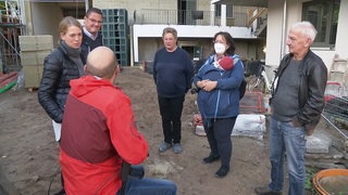 Die Beteiligten eines alternativen Bauprojekts in der Neustadt stehen auf der Baustelle und unterhalten sich.