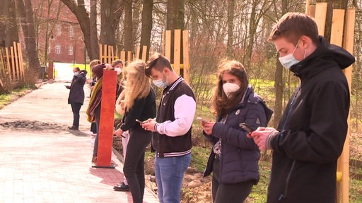Jugendliche mit einem digitalen Projekt in der Burgallee in Hagen im Bremischen. Sie stehen in einer Reihe und haben ihre Smartphones in den Händen.
