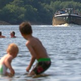 Kinder spielen in der Weser am Café Sand, im Hintergrund kommt ein Lastenschiff