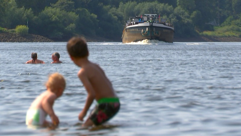 Kinder spielen in der Weser am Café Sand, im Hintergrund kommt ein Lastenschiff