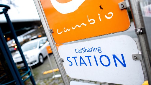 Ein Schild mit der Aufschrift "CarSharing Station" steht an einem Parkplatz, der für Fahrzeuge des Anbieters Cambio reserviert ist.