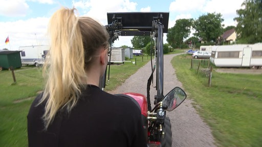 Reporterin Finja Böhling fährt einen Traktor auf einem Campingplatz.