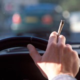 Eine Person sitzt am Steuer eines Autos und hält einen Joint in der Hand.