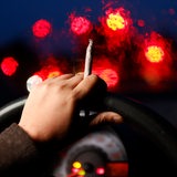 Ein Joint mit Tabak wird am Auto-Lenkrad gehalten
