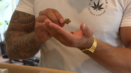 Eine Hand hält ein Stück Cannabis hoch. 