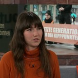 Eine Frau mit dunklen Haaren und orangenem Pullover im Studio von buten un binnen.
