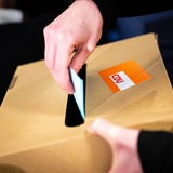 Eine Hand steckt einen Stimmzettel in einen Karton mit einem CDU-Aufkleber.