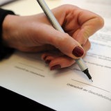 Eine Frauenhand unterschreibt als Geschäftsführerin einen Vertrag.