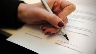 Eine Frauenhand unterschreibt als Geschäftsführerin einen Vertrag.