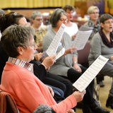Mehrere Menschen mit Notenblättern singen im Chor.