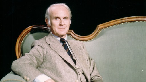 Vicco von Bülow sitzt auf einem grünen Sofa