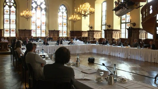 In der oberen Rathaushalle sitzen Vertreter aus Politik und Wirtschaft an einem langen Tischkarree