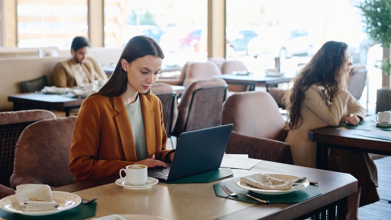 Eine junge Frau sitzt in einem Restaurant und arbeitet an ihrem Laptop.