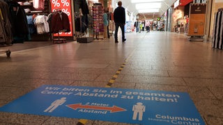 Blick in eine Ladenzeile, auf dem Boden weist ein Schild auf den Abstand von 1,5 Metern hin.