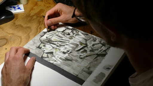 Ein Mann sitzt an einem Schreibtisch und zeichnet an einem Bild.
