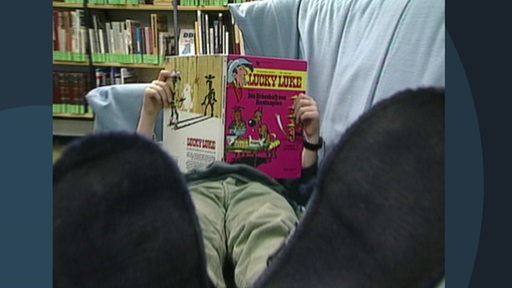 Ein Kind liegt auf dem Sofa einer Bibliothek und ließt ein Comic.