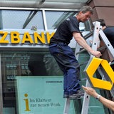 Ein Bauarbeiter befestigt das Commerzbanklogo an einer Filiale