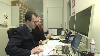 Zwei Personen sitzen in einem Büro an einem Computer.