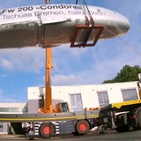 Die über zwanzig Jahre von Rentnern restaurierte Condor-Maschine ist auf einem LKW in Richtung Berlin unterwegs. Davor stehen die Beteiligten um sich zu verabschieden.