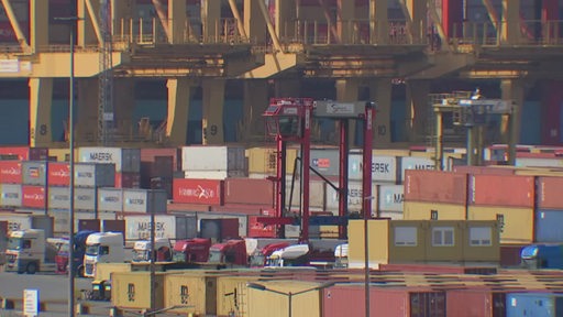 Es sind mehrere Container und LKW´s an einem Hafen zu sehen.