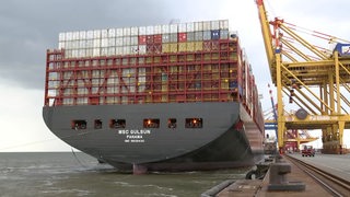 Ein riesiges Containerschiff an der einer Kaje mit Kränen.