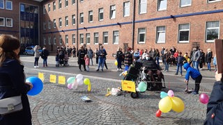 Menschen stehen mit Luftballons und Plakaten vor einem Haus.
