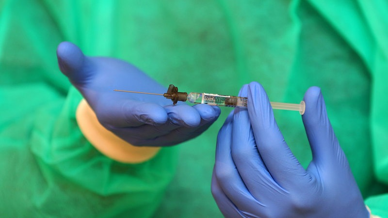 Ein Mensch im Schutzanzug hält eine Impfspritze (Symbolbild)