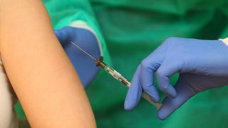 Eine Person spritzt einer anderen Person einen Corona-Impfstoff.