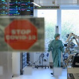 Eine Intensivpflegerin läuft in der Corona-Intensivstation eines Krankenhauses über den Gang während im Vordergrund ein Schild mit der Aufschrift «Stop Covid-19» an der Tür zu sehen ist.