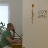 Hausarzt Holger Schelp sitzt am Bürotisch in seinem Sprechzimmer und telefoniert.