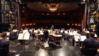 Musiker sitzen auf einer Bühne vor einem leeren Theatersaal.