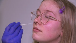 Eine Frau bekommt einen Teststab in die Nase geschoben.