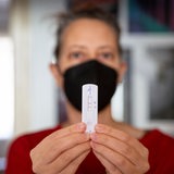 Eine Frau hält einen positiven Corona-Test in die Luft