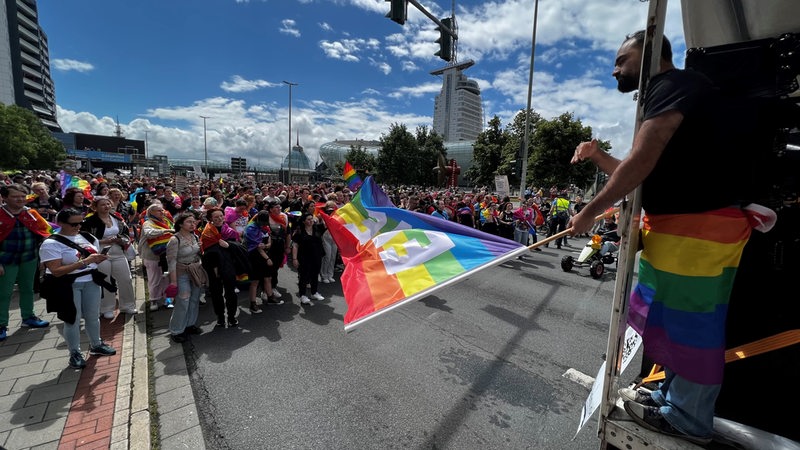 Ein Mann in Bremerhaven schwenkt eine Regenbogenflagge beim CSD