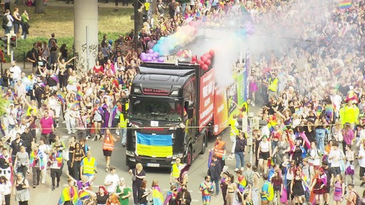 Ein bunter Truck fährt in der Mitte einer großen Demonstration des Christopher Street Days in Bremen neben vielen Menschen.