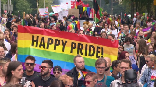 Viele Menschen demonstrieren mit einer großern Regenbogen "happy pride" Flagge beim CSD.