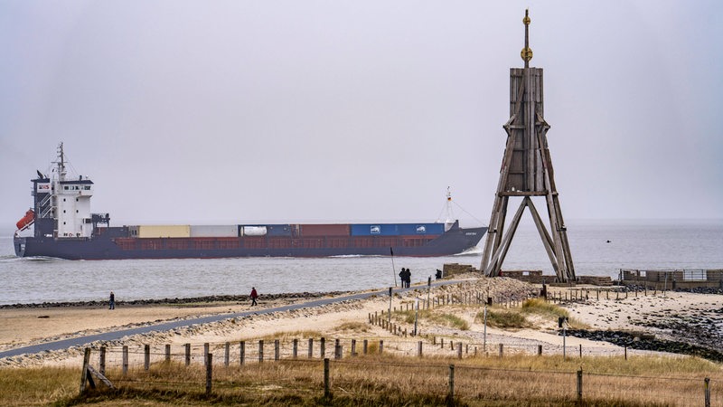 Hinter der Kugelbake in Cuxhaven fährt ein Containerschiff übers Wasser.