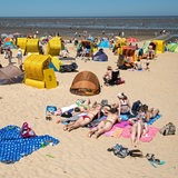 Zahlreiche Menschen halten sich mit Strandkörben und Strandmuscheln an einem Strand vor dem Wattenmeer auf.