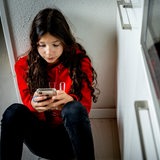 Eine Schülerin sitzt auf dem Boden und schaut unglücklich auf ihr Smartphone