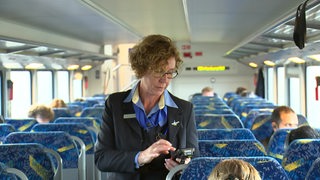 In einem Zugabteil in einer Regionalbahn ist eine Ticketkontrolleurin zu sehen.