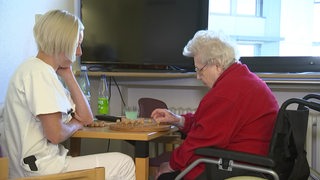 Eine Pflegerin und eine alte Dame spielen ein Brettspiel