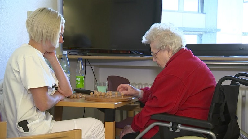 Eine Pflegerin und eine alte Dame spielen ein Brettspiel