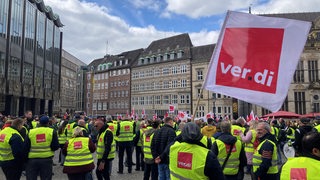 Auf dem Bremer Marktplatz vor der Bremischen Bürgerschaft stehen zahlreiche Menschen mit gelben Warnwesten, auf denen "Verdi" steht. Eine Person schwenkt eine Verdi-Flagge.
