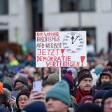 Auf einer Demonstration gegen die AfD ist das Plakat zu lesen: "Nie wieder Faschismus-AfD-Verbot. Jetzt Demokratie verteidigen!" Eine Uhr zeigt auf 5 nach 12.