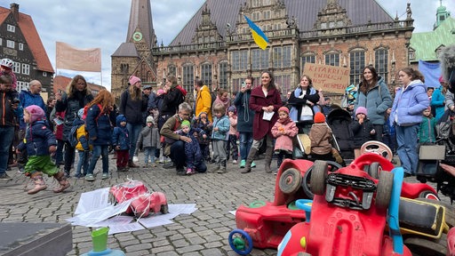 Kinder, Eltern und Erzieherinnen bei einer Demonstration auf dem Bremer Marktplatz, im Vordergrund gestapelte Rutschautos