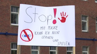 Ein Plakat, welches auf einer Demo gegen die Maskenpflicht eingesetzt wird. Darauf die Worte "Stop! Mit Maske kann ich nicht lernen und spielen."
