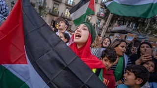 Menschen stehen auf einem Platz und halten Palästina-Flaggen.
