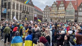 Menschen mit ukrainischen Fahnen stehen in der Bremer Innenstadt
