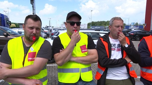 Mitarbeitende mit gelben Warnwesten streiken im Bremerhavener Hafen für bessere Bezahlung und angemessene Arbeitszeiten