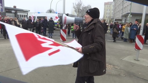 Zu sehen ist ein Demonstrant mit Megaphon in der Hand, der eine Rede für die Demonstranten hält